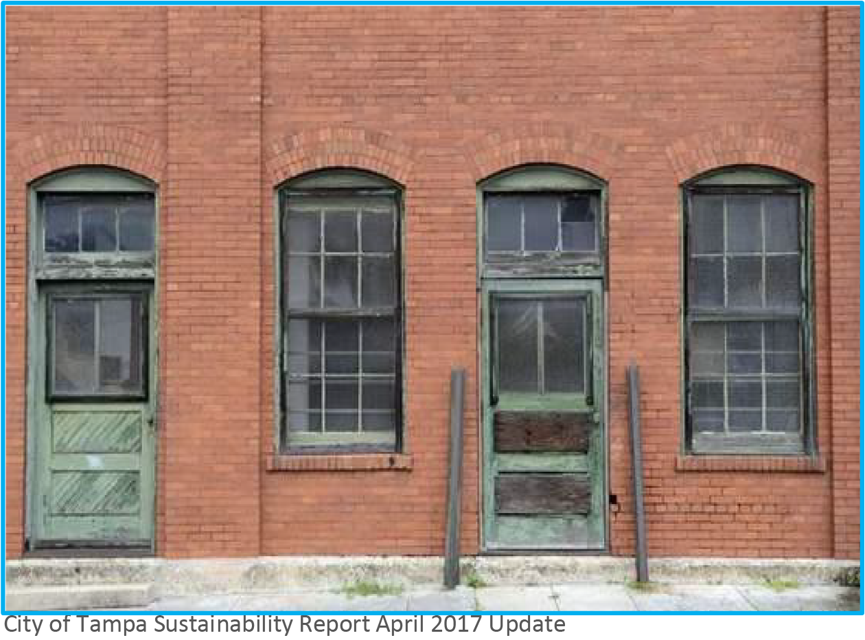 Abandoned brick building featuring three arched windows and two wooden doors, showing peeling paint and a weathered appearance.