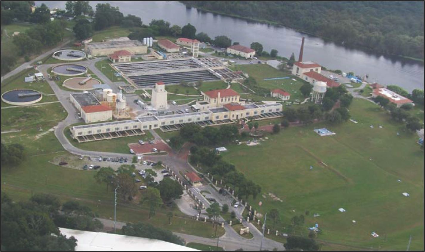 Aerial view of a facility with water treatment plants, green lawns, and a river in the background.