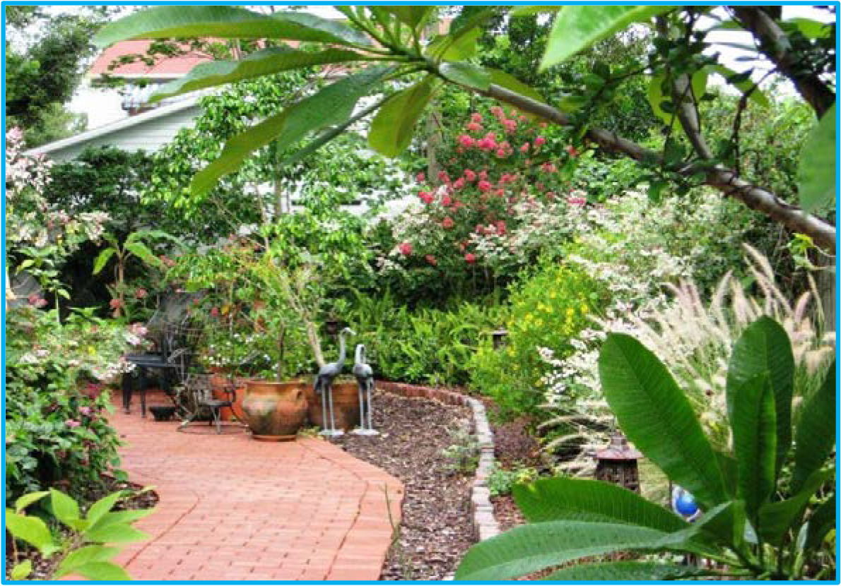 A lush garden pathway with flowering plants, a stone border, and seating areas amidst greenery and vibrant blossoms.