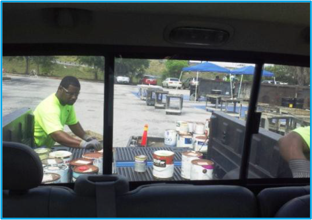 A man in a green shirt organizes paint cans in the back of a truck at an outdoor work site.