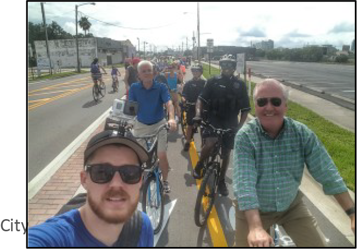 A group of cyclists, including men in casual attire and a police officer, riding along a city street.