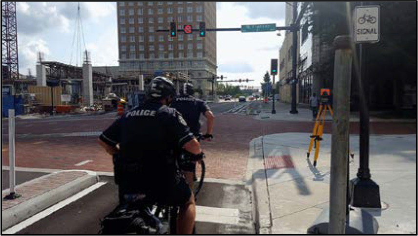 Two police officers on bicycles at an intersection, with construction and traffic signals in the background.