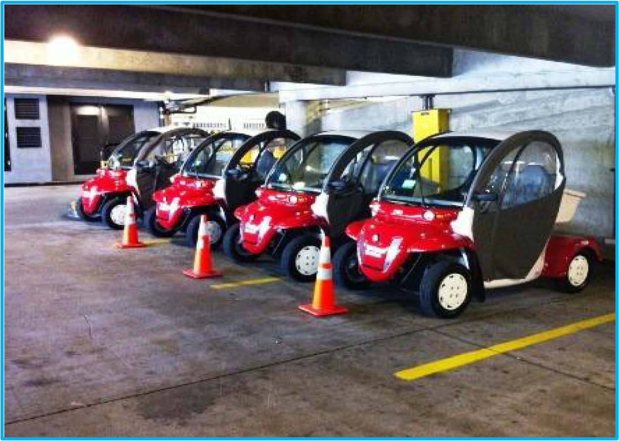 Five red electric carts parked in a garage lined with orange traffic cones.