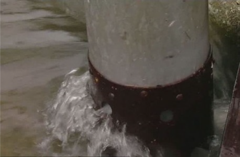 A metal post with a rusted base partially submerged in water, with small waves gently lapping around it.